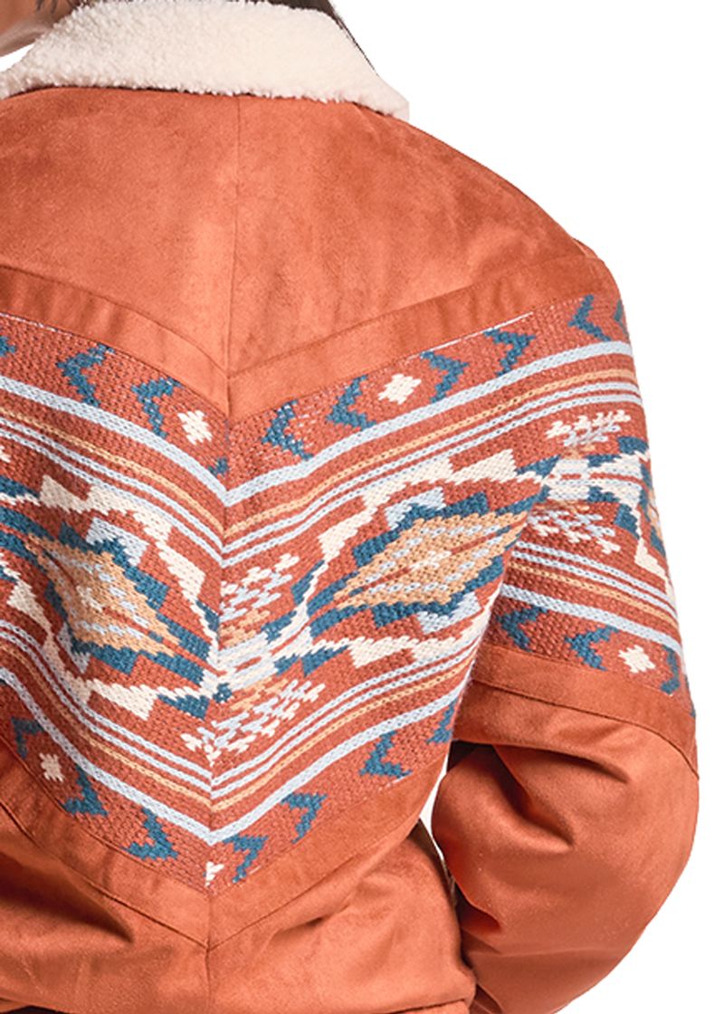 Close-up of the back of a rust-orange suede jacket with a cream sherpa collar and a large Southwestern-style geometric patterned panel in blue, beige, and white.