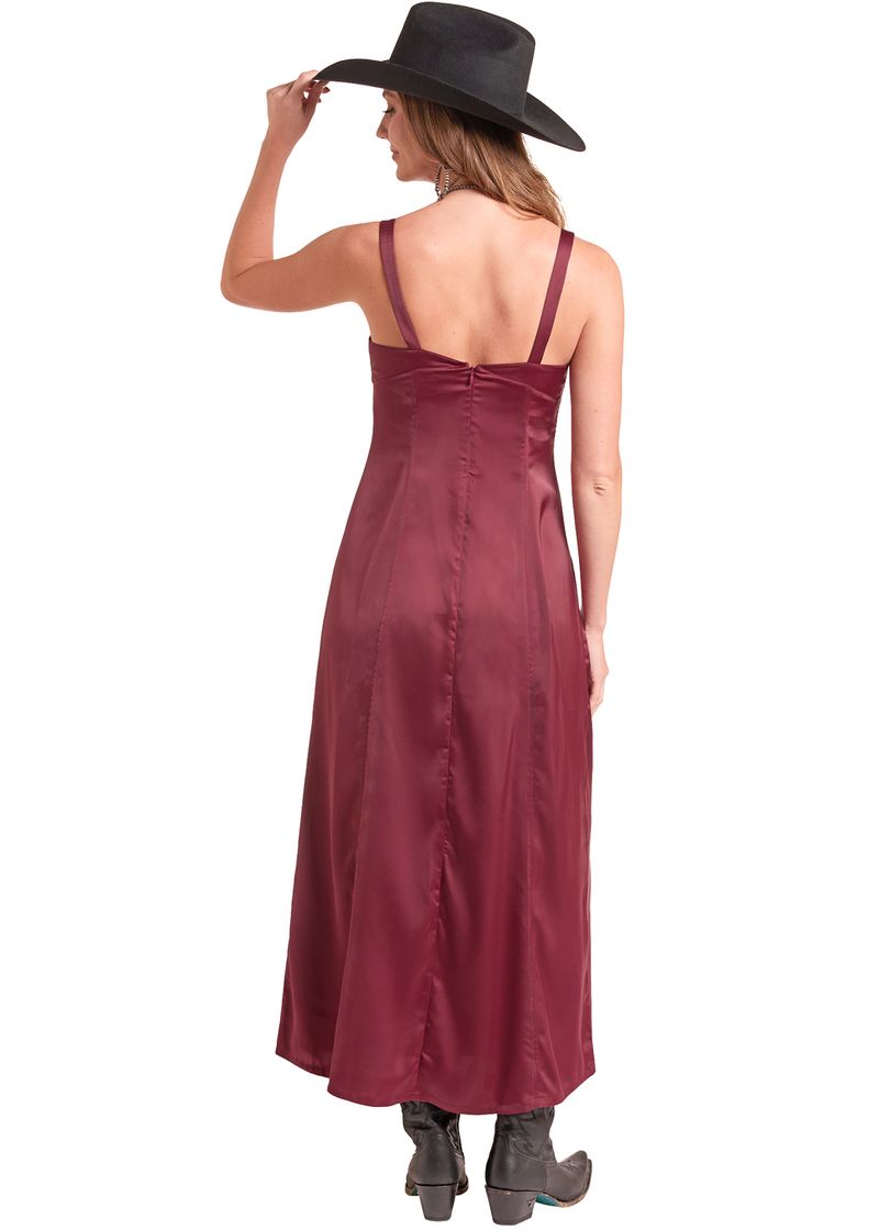 A woman shown from the back wearing a long burgundy satin slip dress with spaghetti straps, a black wide-brim hat, and black boots, set against a plain white background.