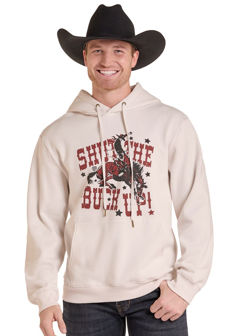 A man wearing a cream-colored hoodie with a western-themed graphic that reads 'SHIT THE BUCK UP!' in red and black.