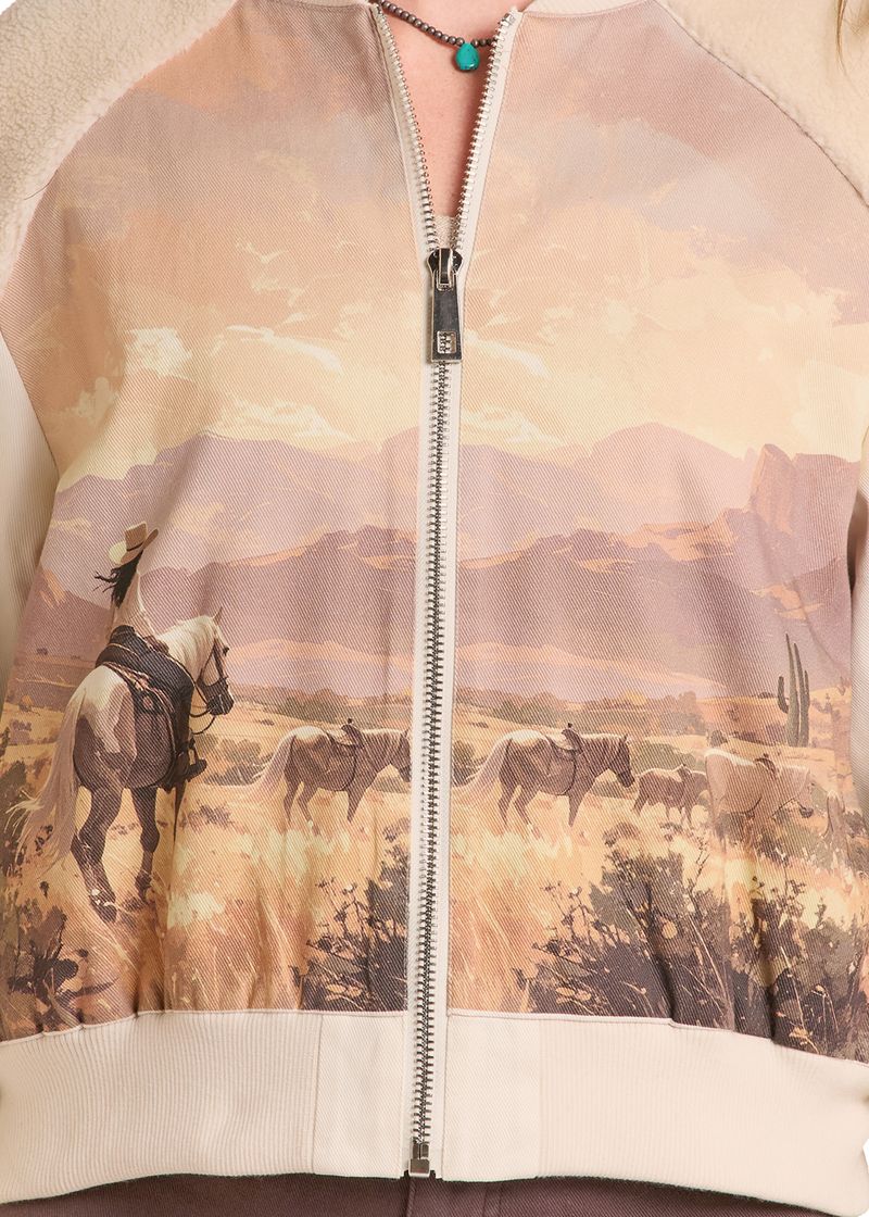 Close-up of a zip-front jacket with a western desert landscape print, featuring a rider on horseback, other horses, mountains, cacti, and cream ribbed trim.