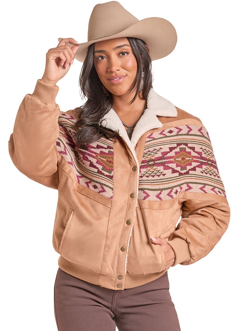 A woman wearing a tan suede western-style jacket with a sherpa fleece collar and a Southwestern patterned yoke, paired with a matching tan cowboy hat and brown pants, against a white background.
