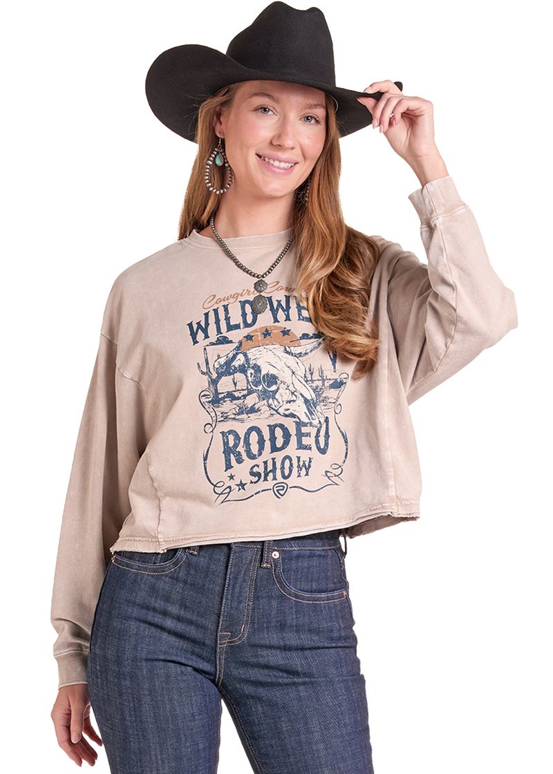 A woman wearing a beige cropped sweatshirt with a blue and orange 'Wild West Rodeo Show' graphic, paired with blue jeans and a black cowboy hat, against a plain white background.